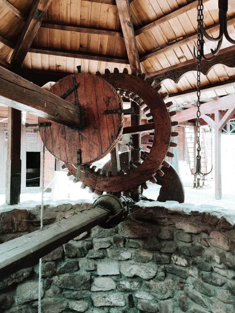 Explore a traditional wooden water wheel set against a rustic village backdrop, showcasing historical engineering.
